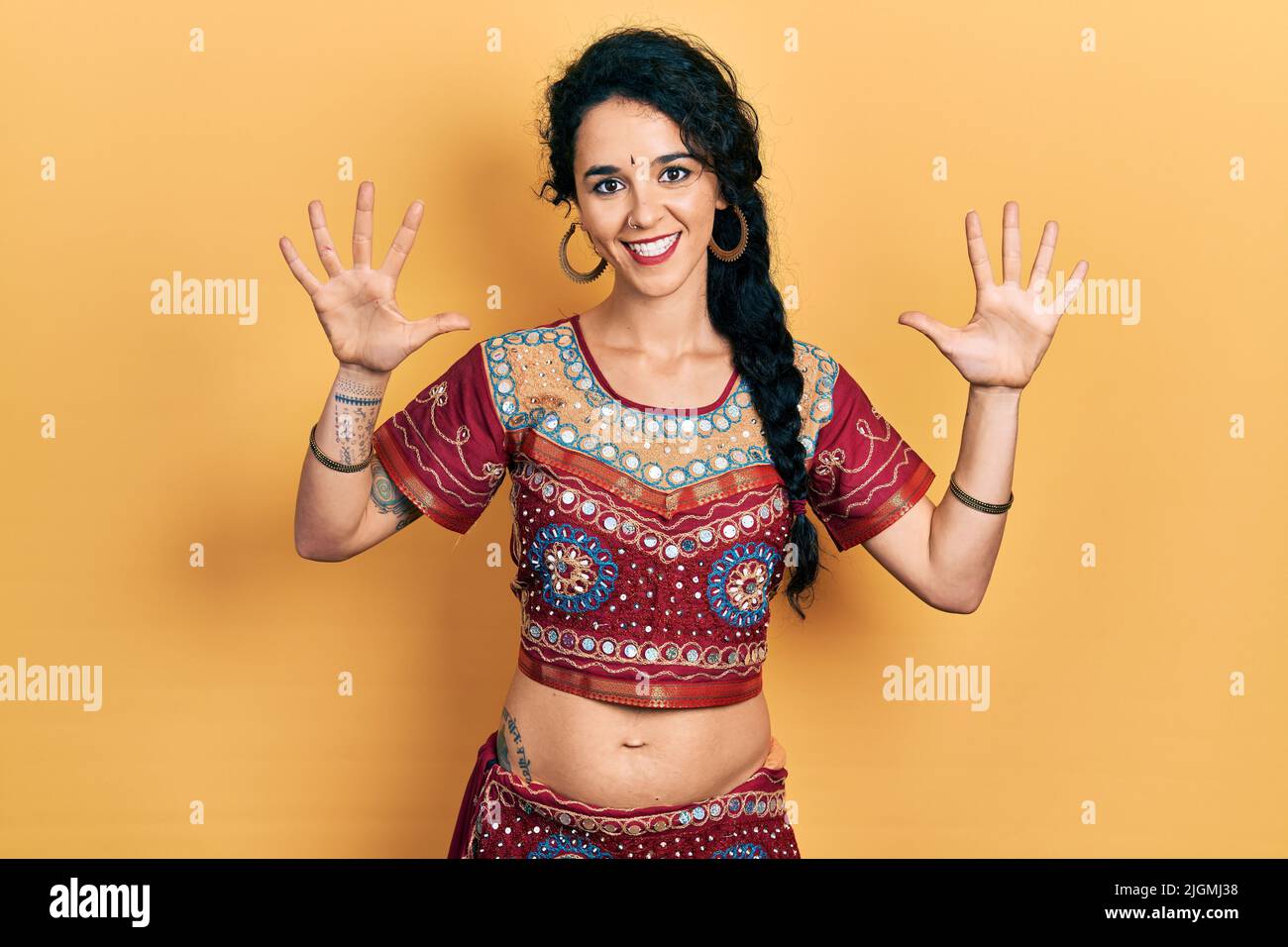 Junge Frau in Bindi- und bollywood-Kleidung zeigt und zeigt mit den Fingern Nummer zehn auf, während sie selbstbewusst und glücklich lächelt. Stockfoto