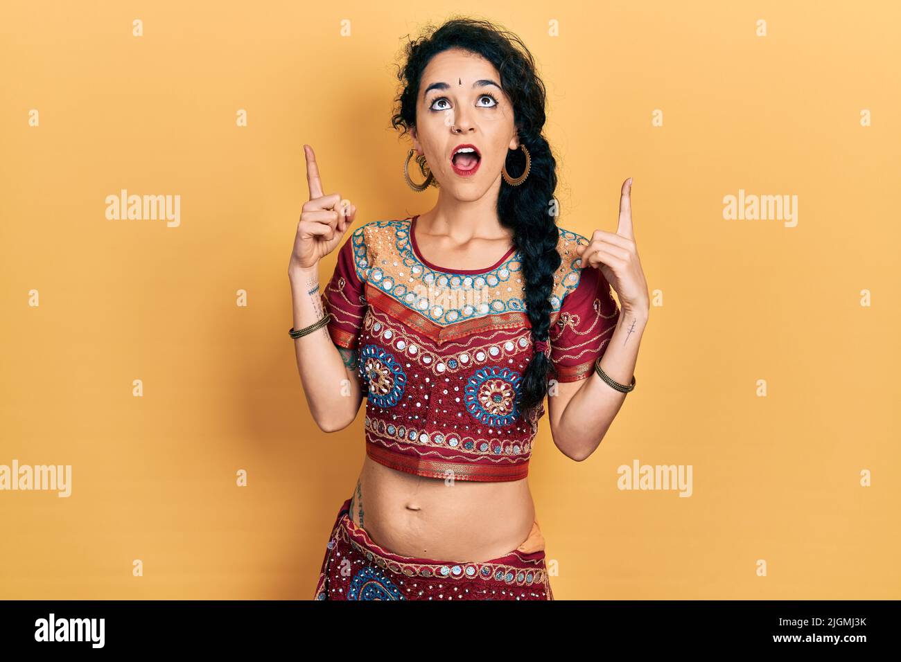 Die junge Frau in Bindi- und bollywood-Kleidung staunte und überraschte mit ihren Fingern und erhobenen Armen nach oben und zeigte. Stockfoto