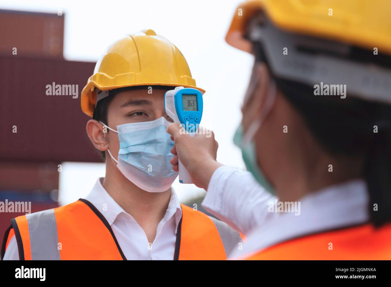asiatischer Arbeiter mit Gesichtsmaske, der Fieber mit einem Digitalthermometer überprüft, bevor er die Arbeit zum Schutz vor Covid, Covid-19 oder Coronavirus p betreten hat Stockfoto