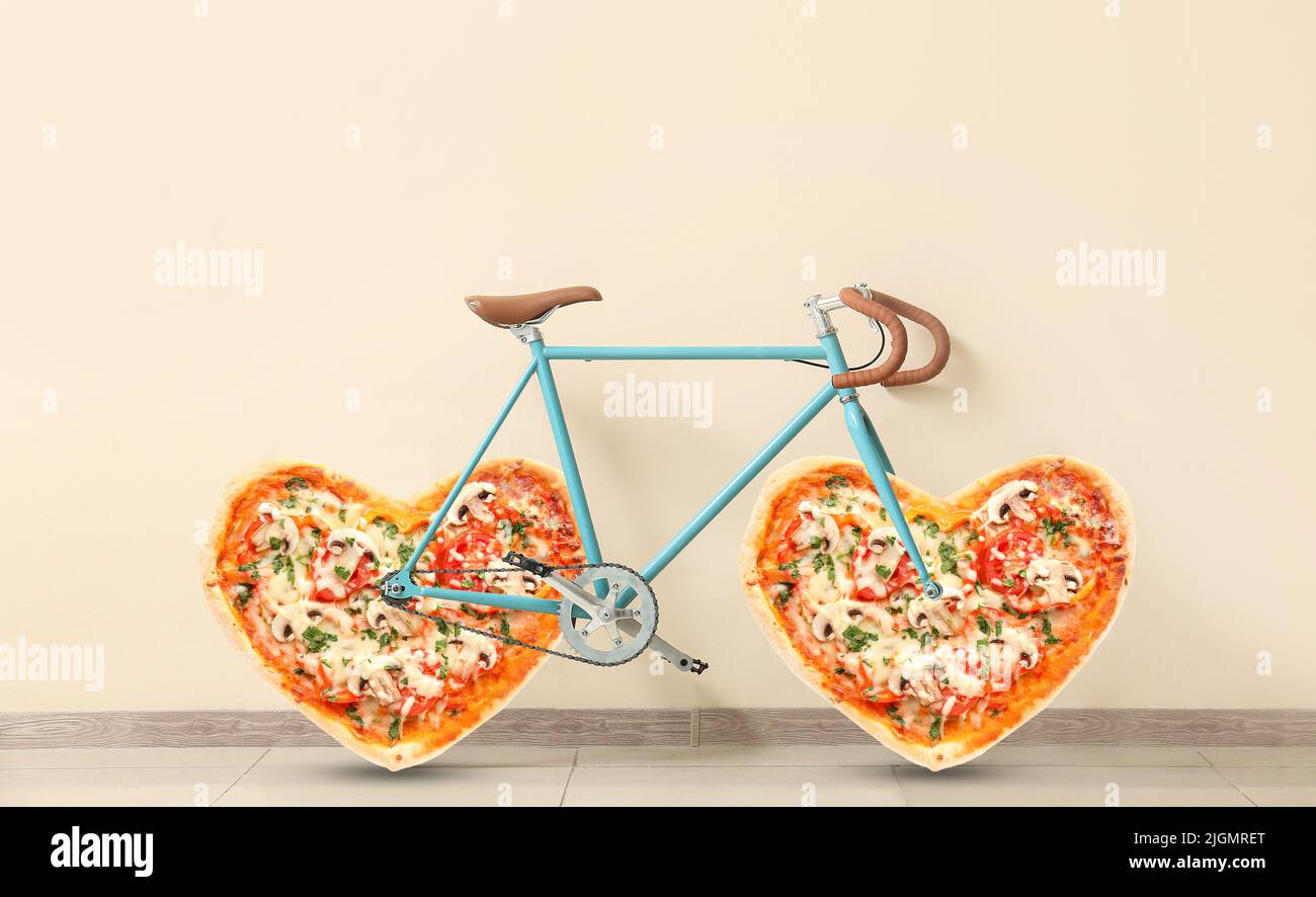 Modernes Fahrrad mit herzförmiger Pizza anstelle von Rädern in der Nähe einer hellen Wand Stockfoto