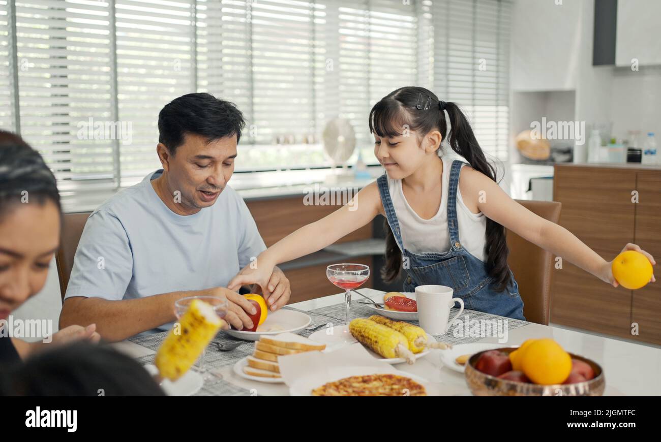 Glückliche asiatische Familie, die am Küchentisch frühstückte, Tochter, die mit dem Vater gesundes Obst servierte. Stockfoto