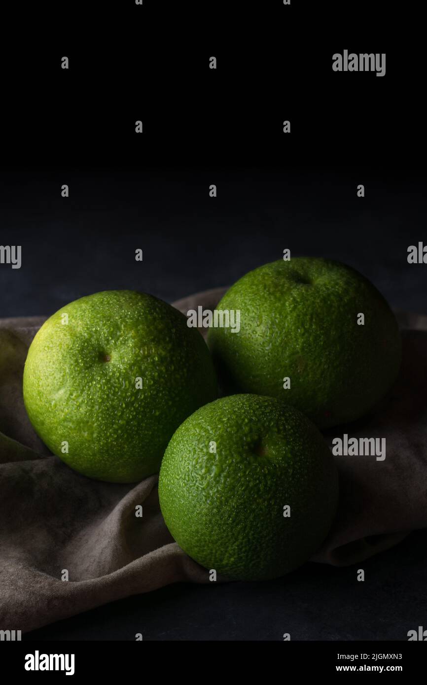 Frisch geerntete, grüne Hautschüppchen, auch Sevilla genannt, sind Zitrusfrüchte mit hohem Vitamin C-Gehalt und Wassertröpfchen auf rustikalem, dunklem Hintergrund mit Kopierraum Stockfoto