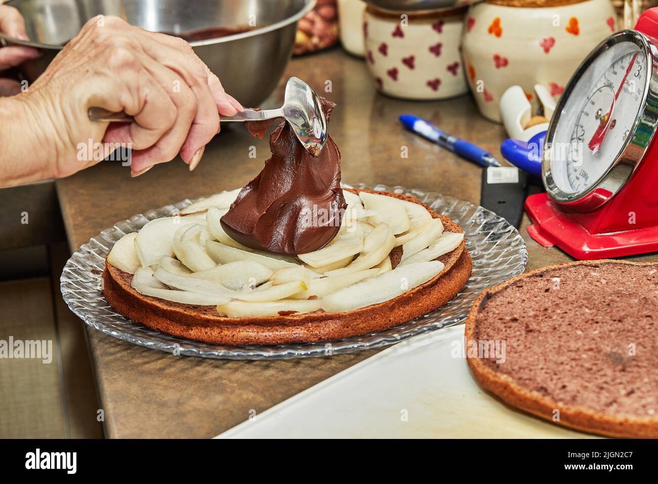 Der Küchenchef legt Schokoladenganache über die Birnen in der Torte, um Schokoladenkuchen mit Birnen und Walnüssen zu machen Stockfoto