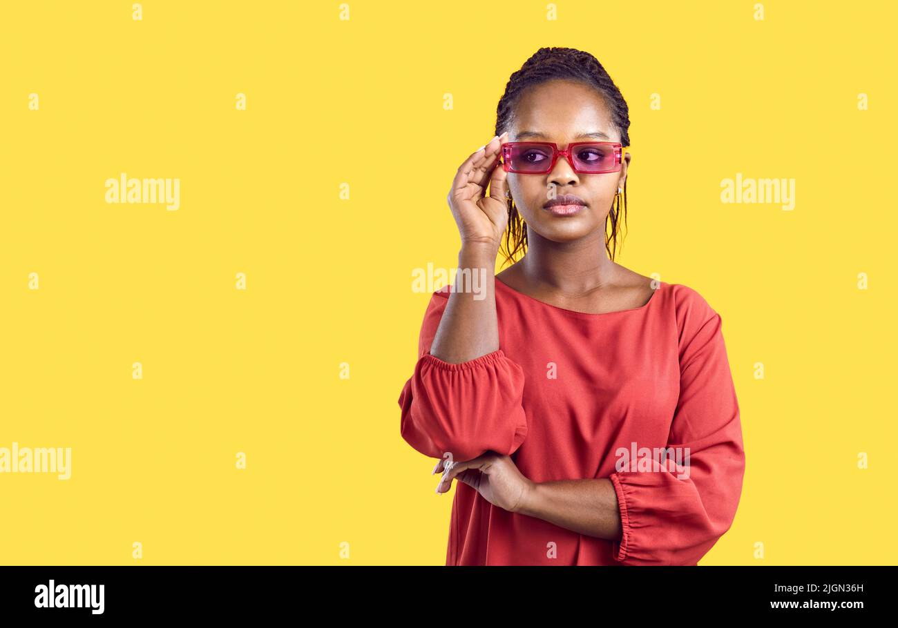 Porträt einer coolen und stilvollen jungen afroamerikanischen Frau in roten Gläsern auf gelbem Hintergrund. Stockfoto