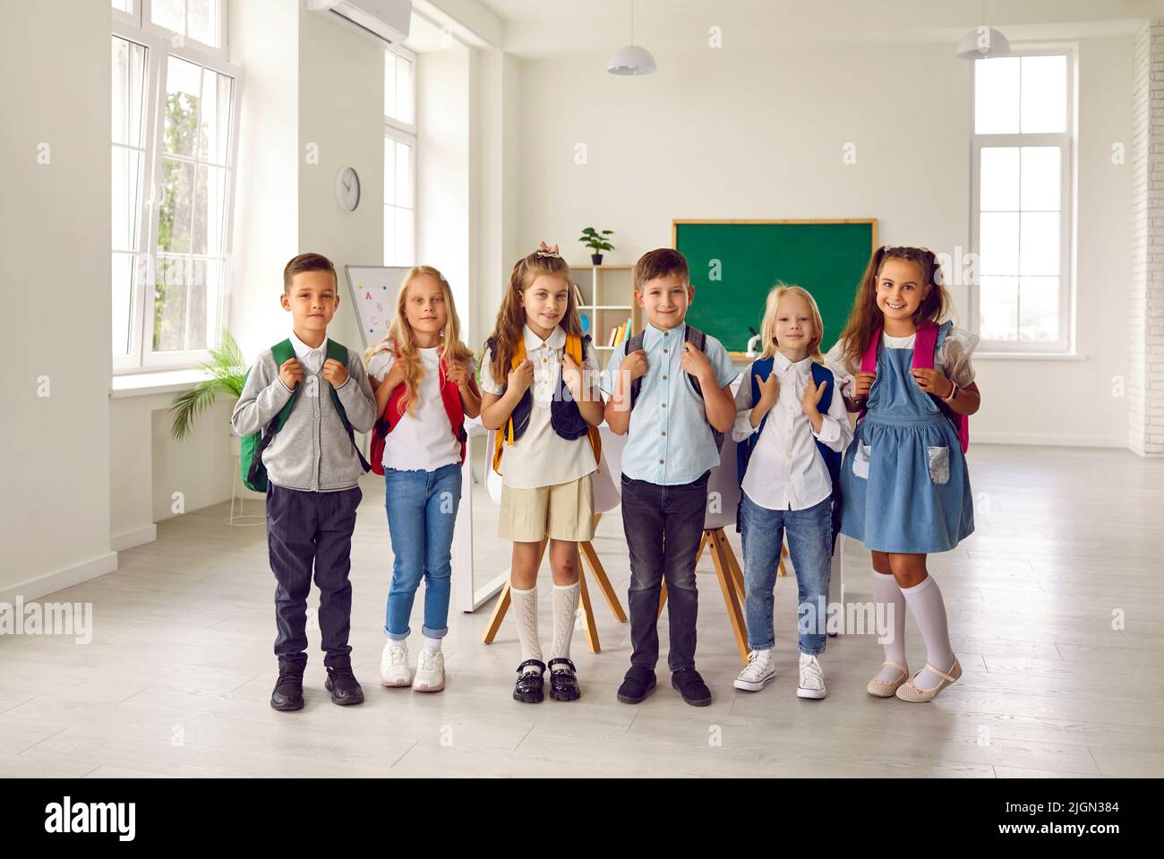 Porträt einer kleinen lächelnden Gruppe von Erstklässlern im modernen Klassenzimmer der Grundschule. Stockfoto