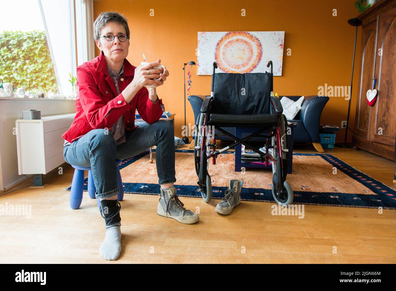 Tilburg, Niederlande. Wohnzimmer Porträt einer erwachsenen Frau mit Multipler Sklerose saß neben ihrem Rollstuhl. Stockfoto