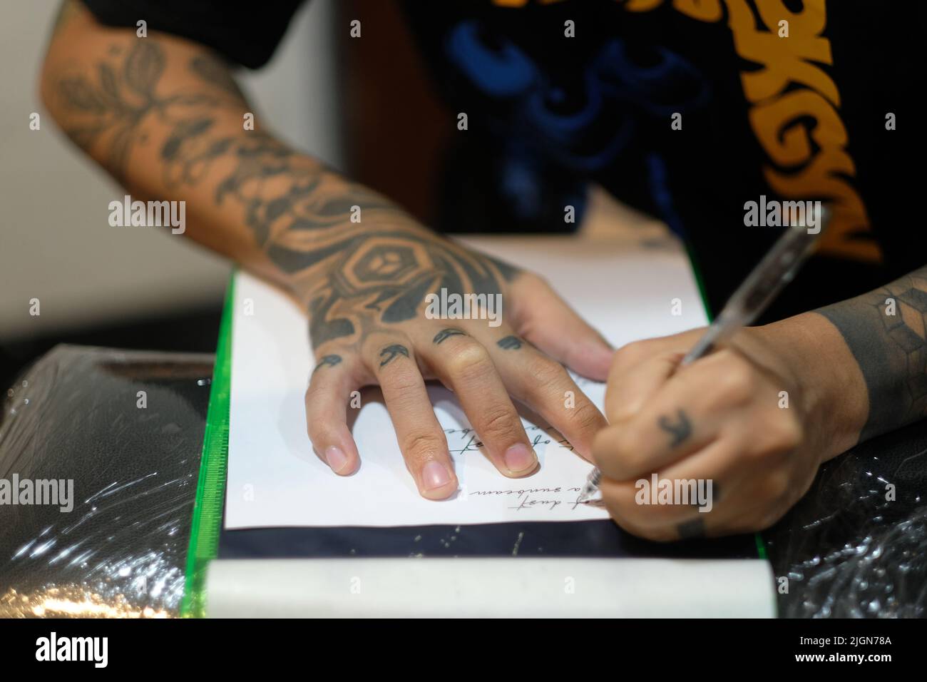 Männlicher Tattoo-Künstler, Arme gefüllt mit eingeklebten Designs, Schablonen kursive Schrift auf weißem Papier mit einem Stift zur Vorbereitung auf eine Tattoo-Sitzung. Stockfoto