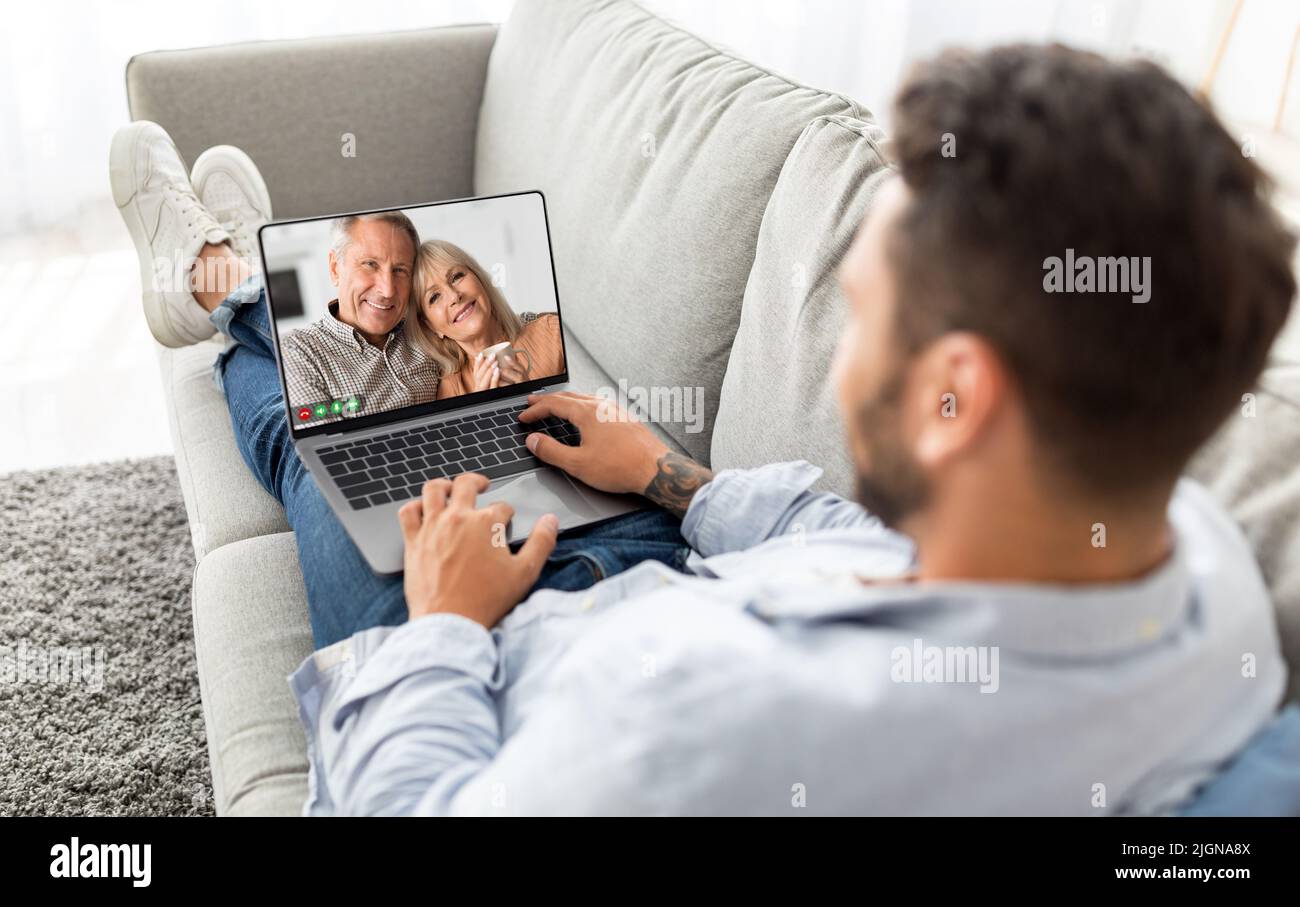 Mann, Der Mit Älteren Eltern Einen Videoanruf Auf Dem Laptop Macht, Während Er Sich Auf Der Couch Entspannt Stockfoto