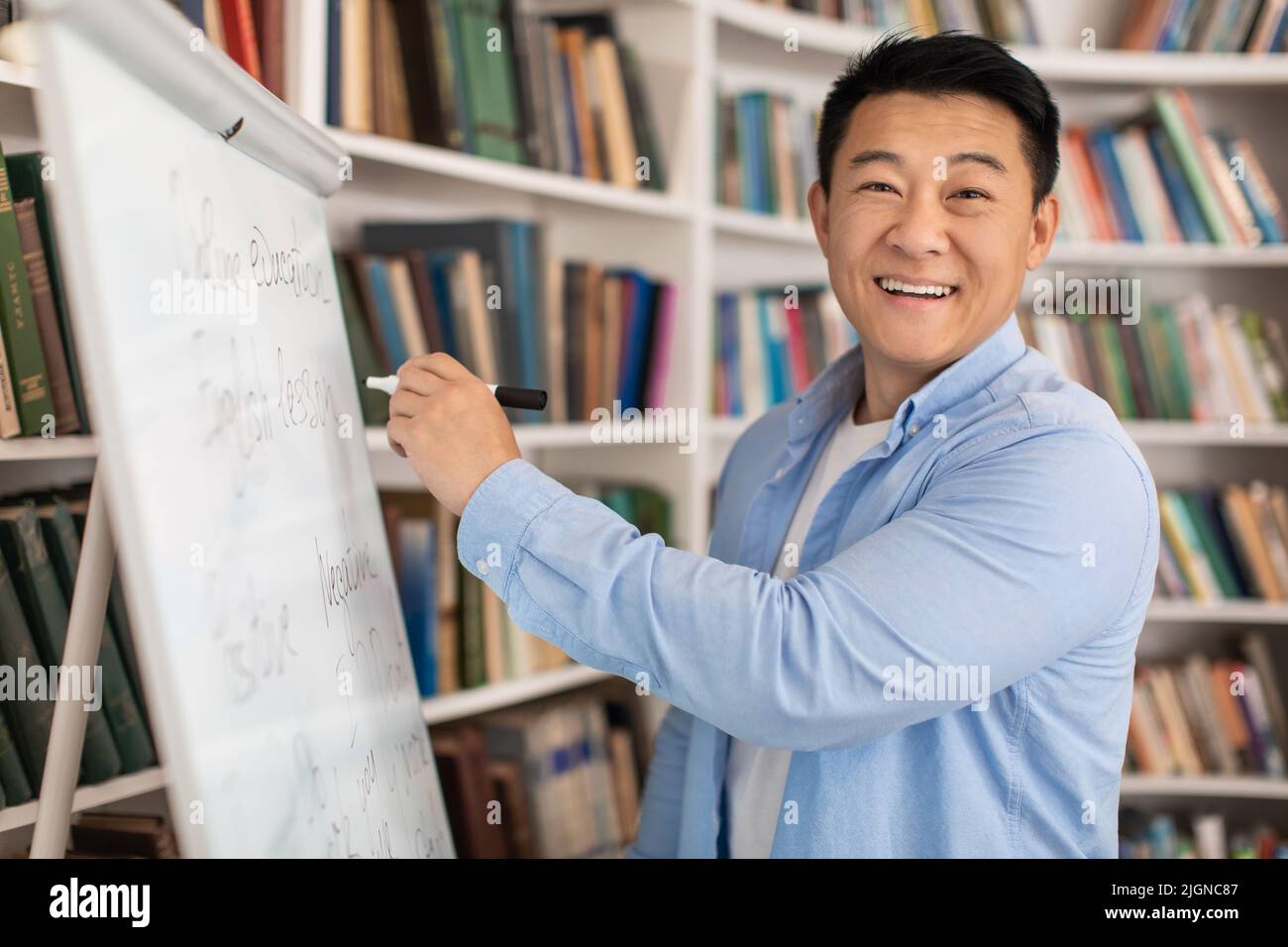 Fröhlicher Japanischer Tutor Mann, Der Auf Whiteboard Schreibt Und Unterricht In Der Halle Hat Stockfoto