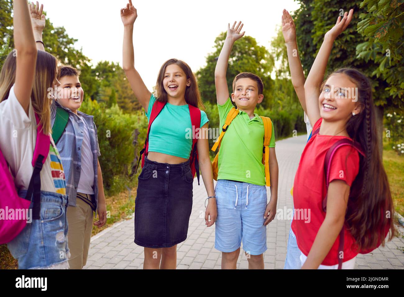 Eine Gruppe kleiner Schulfreunde heben ihre Hände in Luft, nachdem sie sie beim Gehen im Park gestapelt haben. Stockfoto