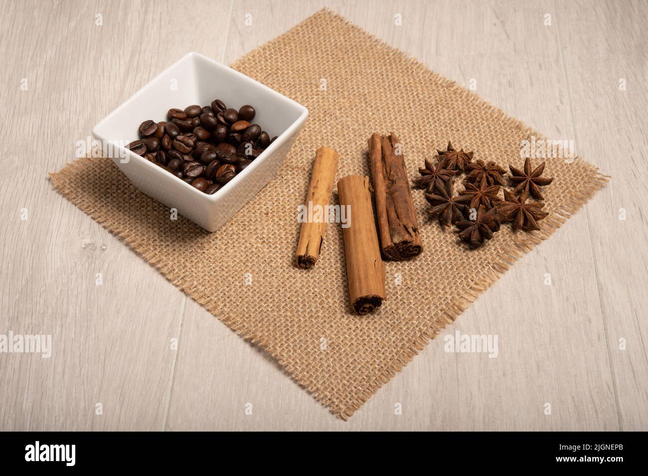 Zimt, Sternanise, Kaffeebohnen aus nächster Nähe auf einem hessischen Tuch mit hellem Holzhintergrund, aufgenommen von oben Stockfoto