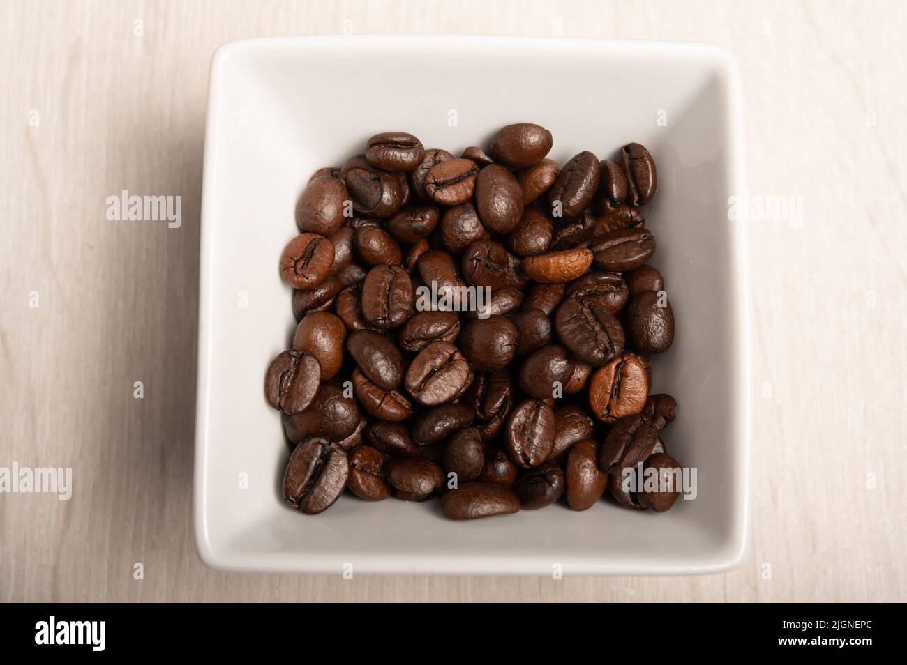 Kaffeebohnen in einer quadratischen weißen Schale auf einem weißen Holzhintergrund, aufgenommen von oben Stockfoto