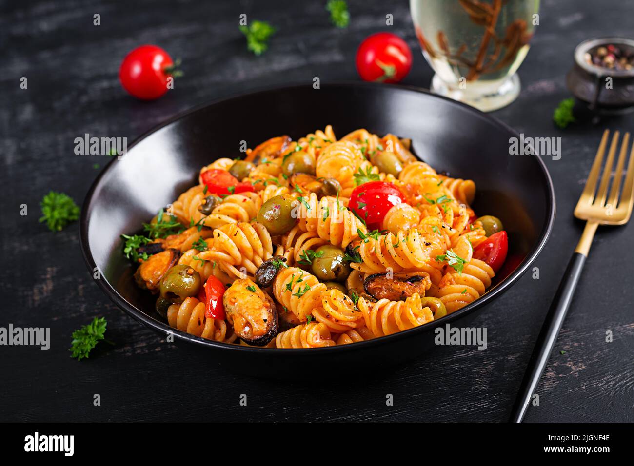 Klassische italienische Pasta fusilli marinara mit Muscheln, grünen Oliven und Kapern auf dunklem Tisch. Fusilli Pasta mit Sauce Marinara Stockfoto