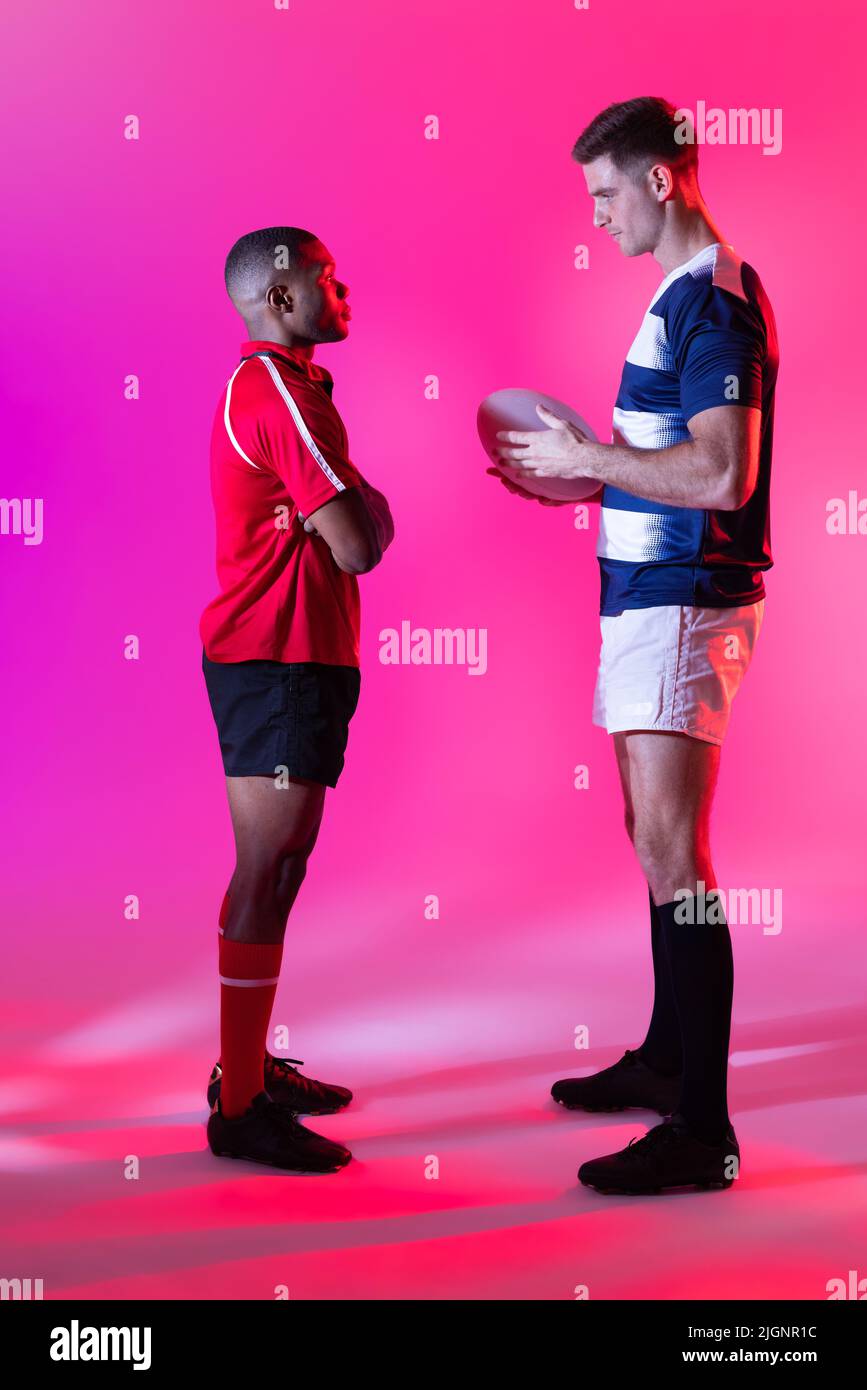 Verschiedene männliche Rugby-Spieler mit Rugby-Ball über rosa Beleuchtung Stockfoto