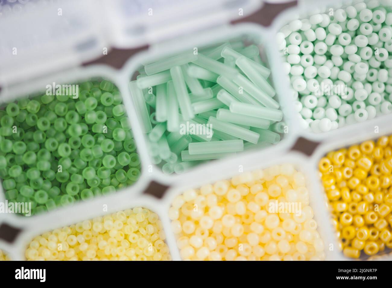 Kleine, kleine bunte Glasperlen im Plastikkastenbehälter Nahaufnahme von oben. Hintergrund und Textur. Stockfoto