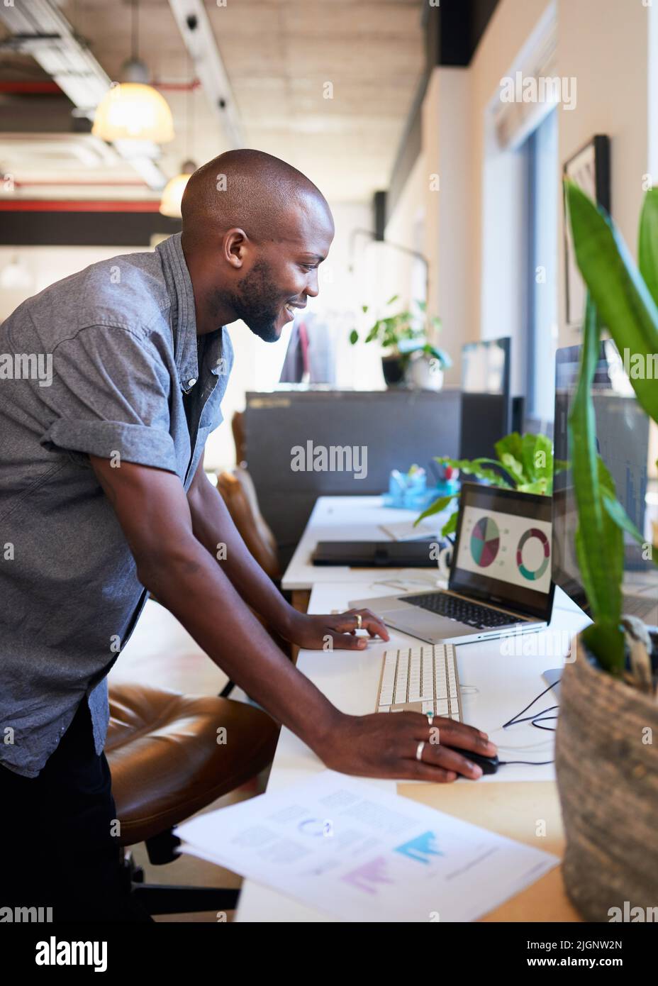 Ein schwarzer Geschäftsmann steht und lehnt sich im Büro über den Schreibtisch Stockfoto