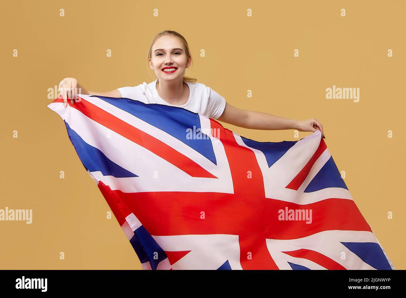 Attraktive blonde Posen mit einer britischen Flagge. Fotoshooting im Studio auf gelbem Hintergrund. Stockfoto