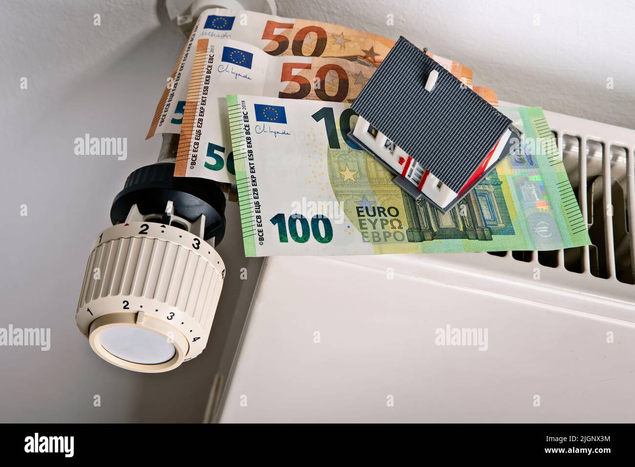 Heizkörper und Thermostat mit Euro-Banknoten und Haus als Symbol für steigende Heizkosten Stockfoto