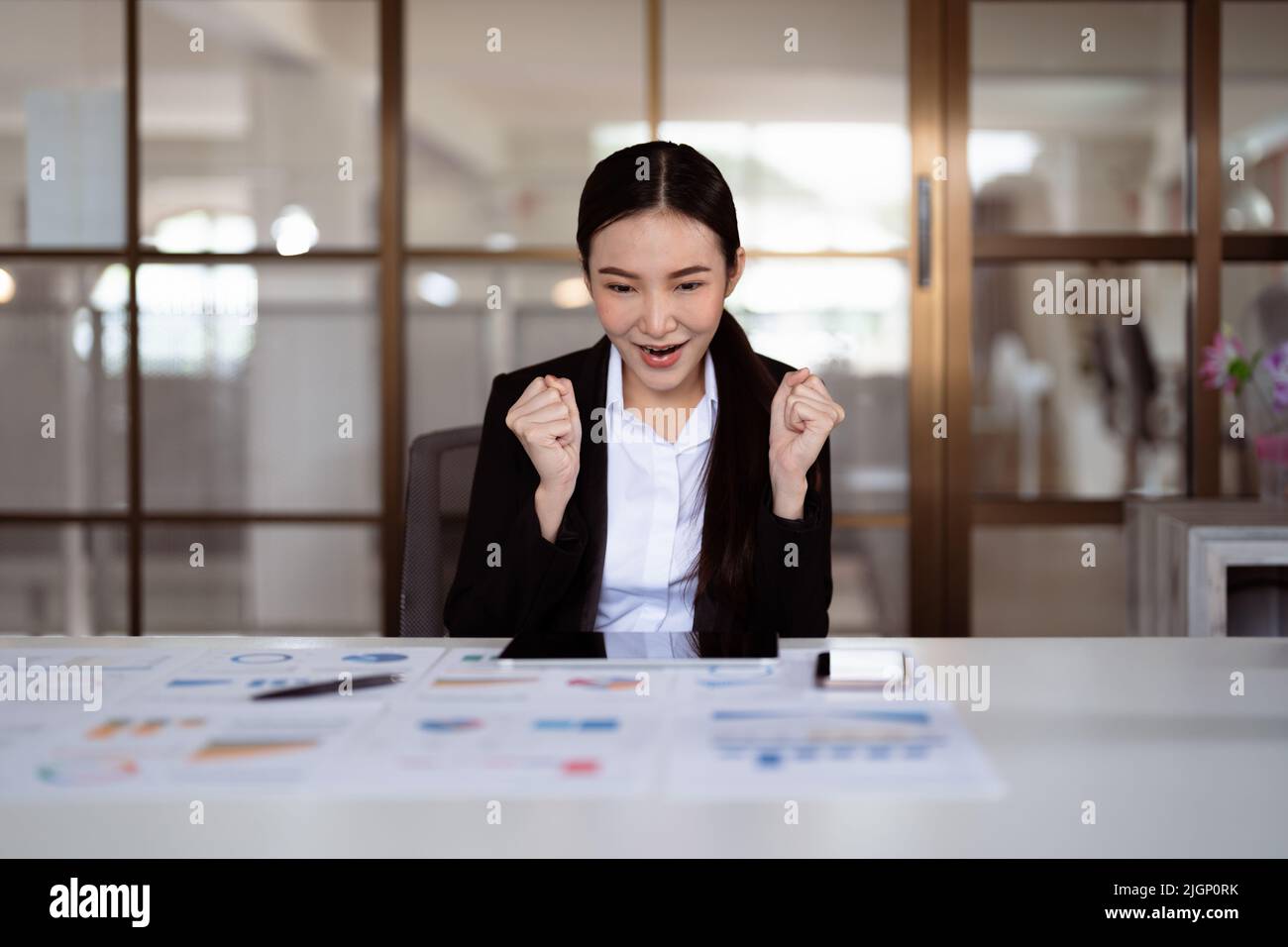 Begeisterte junge asiatische Geschäftsfrau feiert erfolgreiche Finanzprojektergebnisse, zieht wichtige Unternehmenskunden an, Traumziel erreicht. Stockfoto