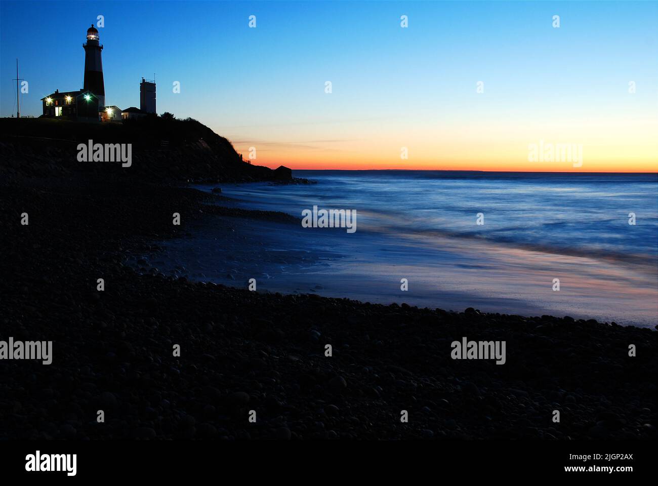 Der Sonnenaufgangshimmel macht den Montauk Point Lighthouse, an der östlichen Spitze von Long Island, New York, in Silhouette, während er sich im Meerwasser spiegelt Stockfoto
