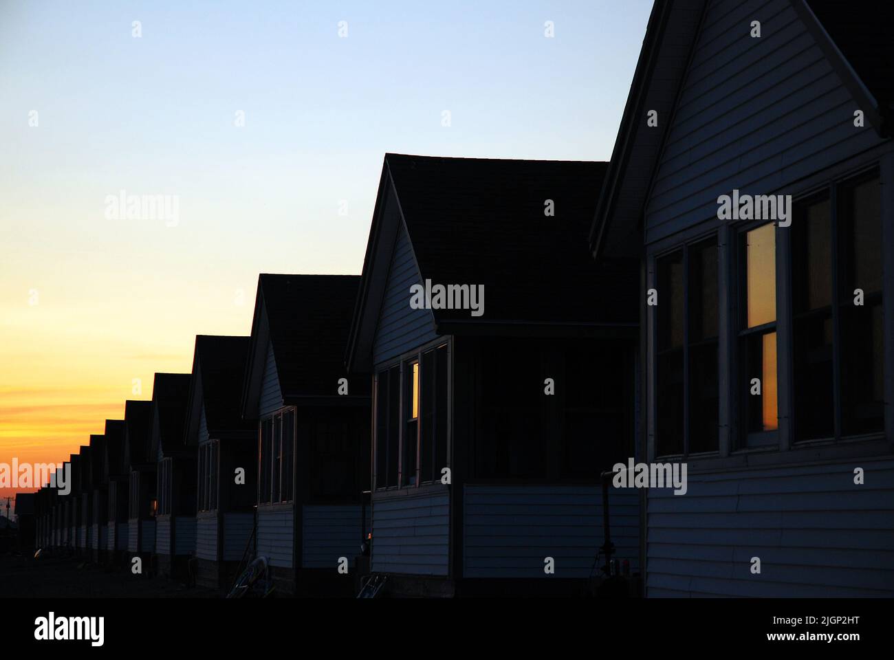 Eine Reihe von identischen bescheidenen kleinen Häusern und Häusern erstrecken sich über den Horizont und reflektieren den Sonnenuntergang Himmel in den Fenstern Stockfoto