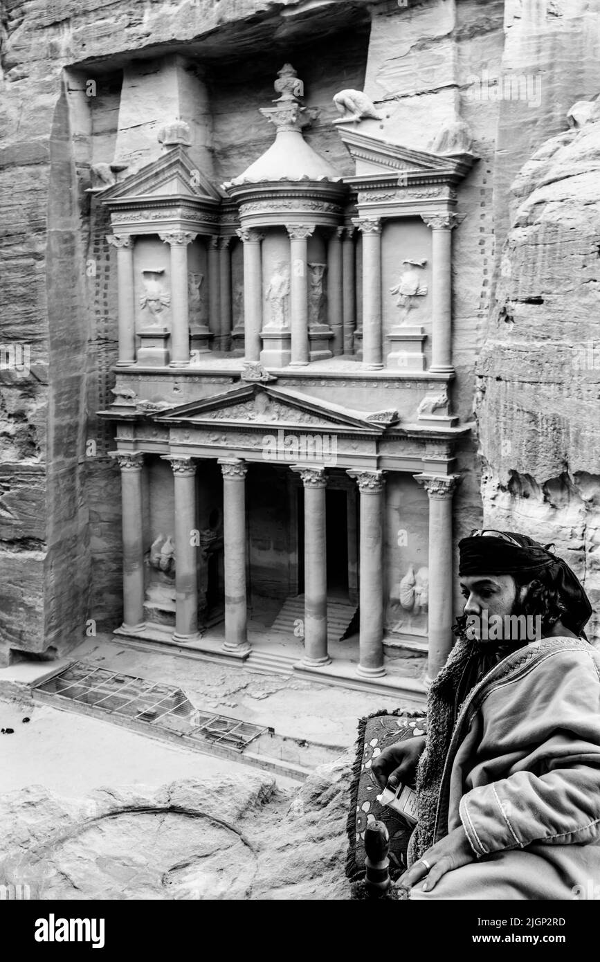 Ein lokaler Beduinenmensch in typischer Kleidung mit dem Äußeren des Schatzhauses ‘Al-Khazneh’ im Hintergrund, Petra, Jordanien. Stockfoto