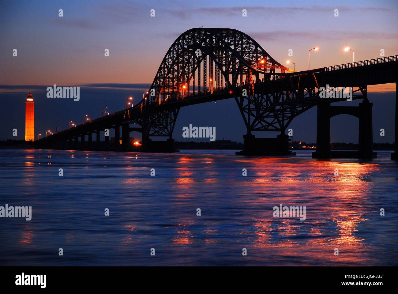 Die Lichter der Stahlbogenbrücke Robert Moses Causeway spiegeln sich im Wasser der Bucht und führen zu einem Leuchtturm auf Long Island Stockfoto