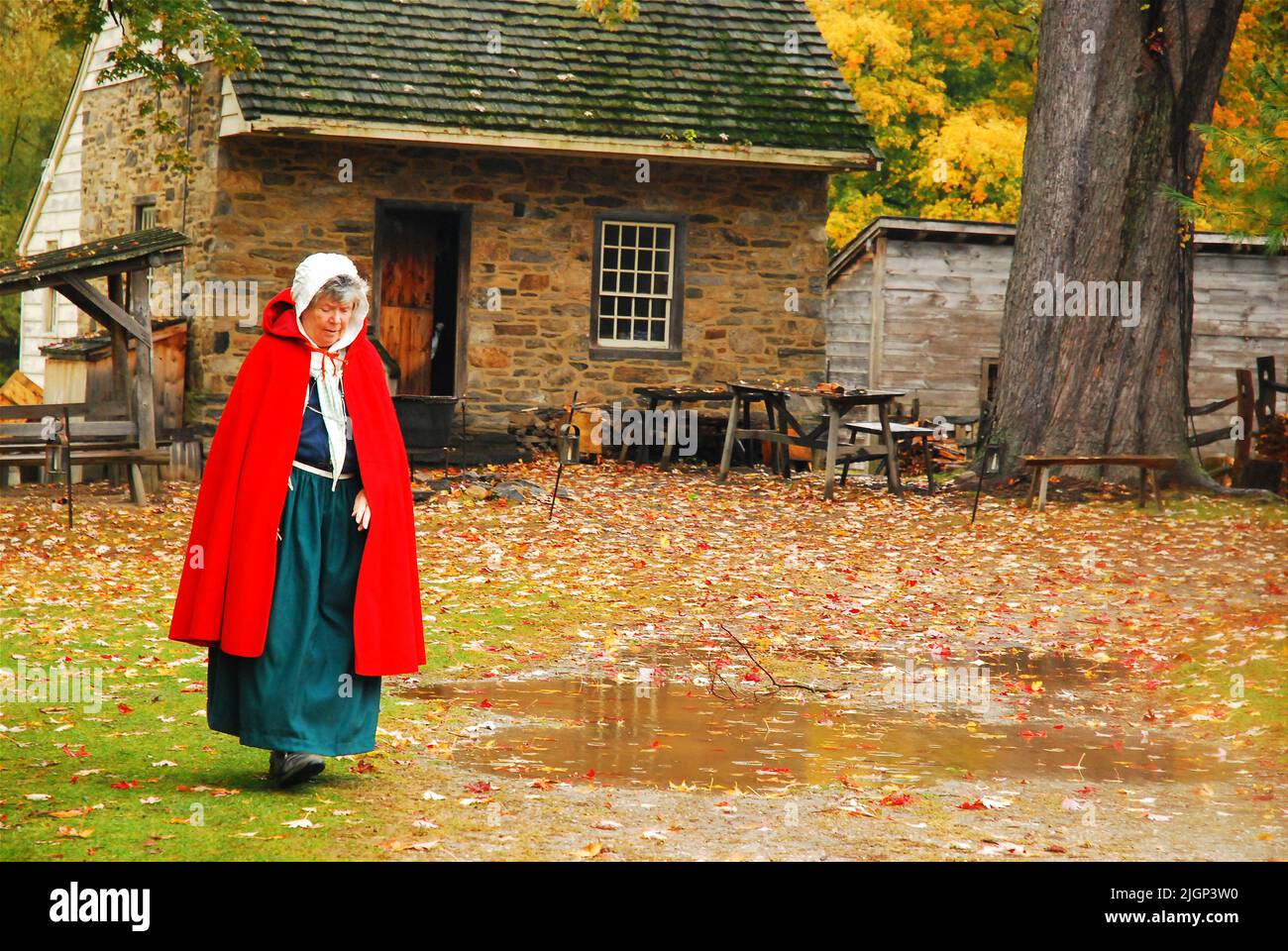 Eine ältere Frau in historischen Kostümen und Kleidern spaziert durch das Phillipsburg Manor, eine nachgebildete holländische Kolonialsiedlung in Westchester County Stockfoto