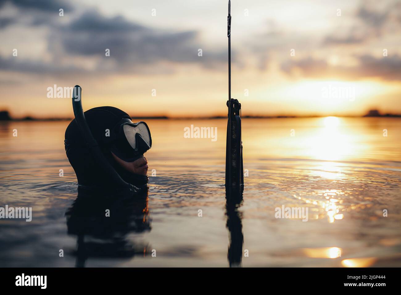 Männlicher Taucher, der eine Speergun hält, während er mitten im Meer in Meerwasser getaucht ist. Taucher, die bei Sonnenuntergang nach Fischen suchen. Stockfoto