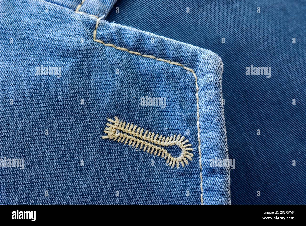 Naturweißes Knopfloch, gestickt auf einer blauen Baumwoll-Sportjacke, Revers mit Spitzenmuster, Nahaufnahme. Hintergrund. Stockfoto