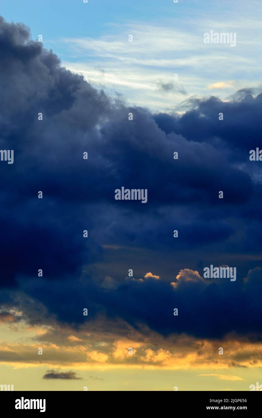 Dramatischer wolkiger blauer Himmel mit grau-blauen und orangen Wolken bei Sonnenuntergang. Natürlicher Hintergrund, Tapete. Vertikale Zusammensetzung. Trencin, Slowakei. Stockfoto