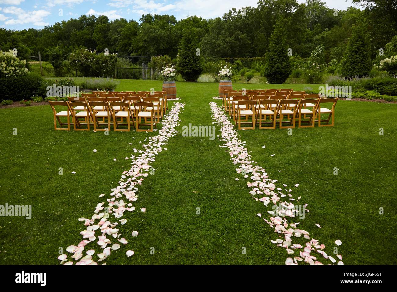 Leere Gästestühle bei einer Hochzeit im Freien auf dem Gras mit Bäumen im Hintergrund. Stockfoto