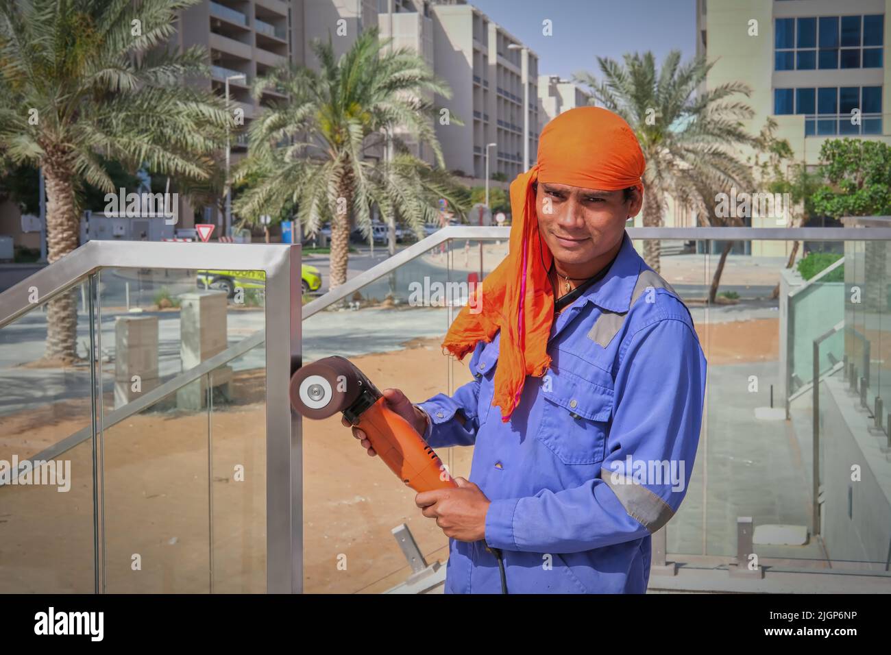 Porträt eines jungen Straßenarbeiters aus dem Nahen Osten mit blauer Uniform und orangefarbenem Kopfschmuck und polierfähigem Polierwerkzeug in den Händen.VAE Stockfoto