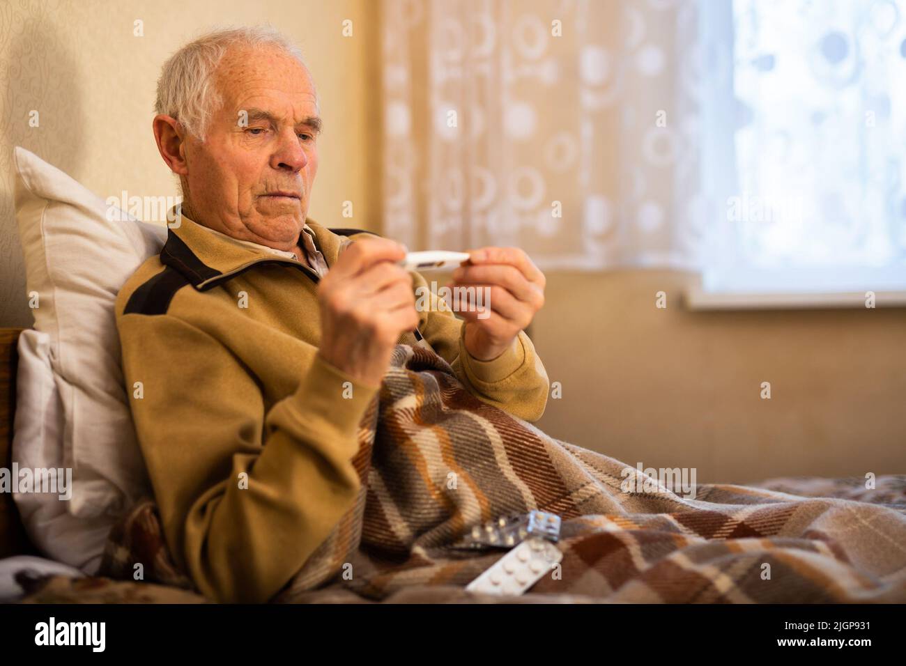 Grauhaariger älterer Mann, der die Körpertemperatur auf dem Thermometer zu Hause ansieht Stockfoto