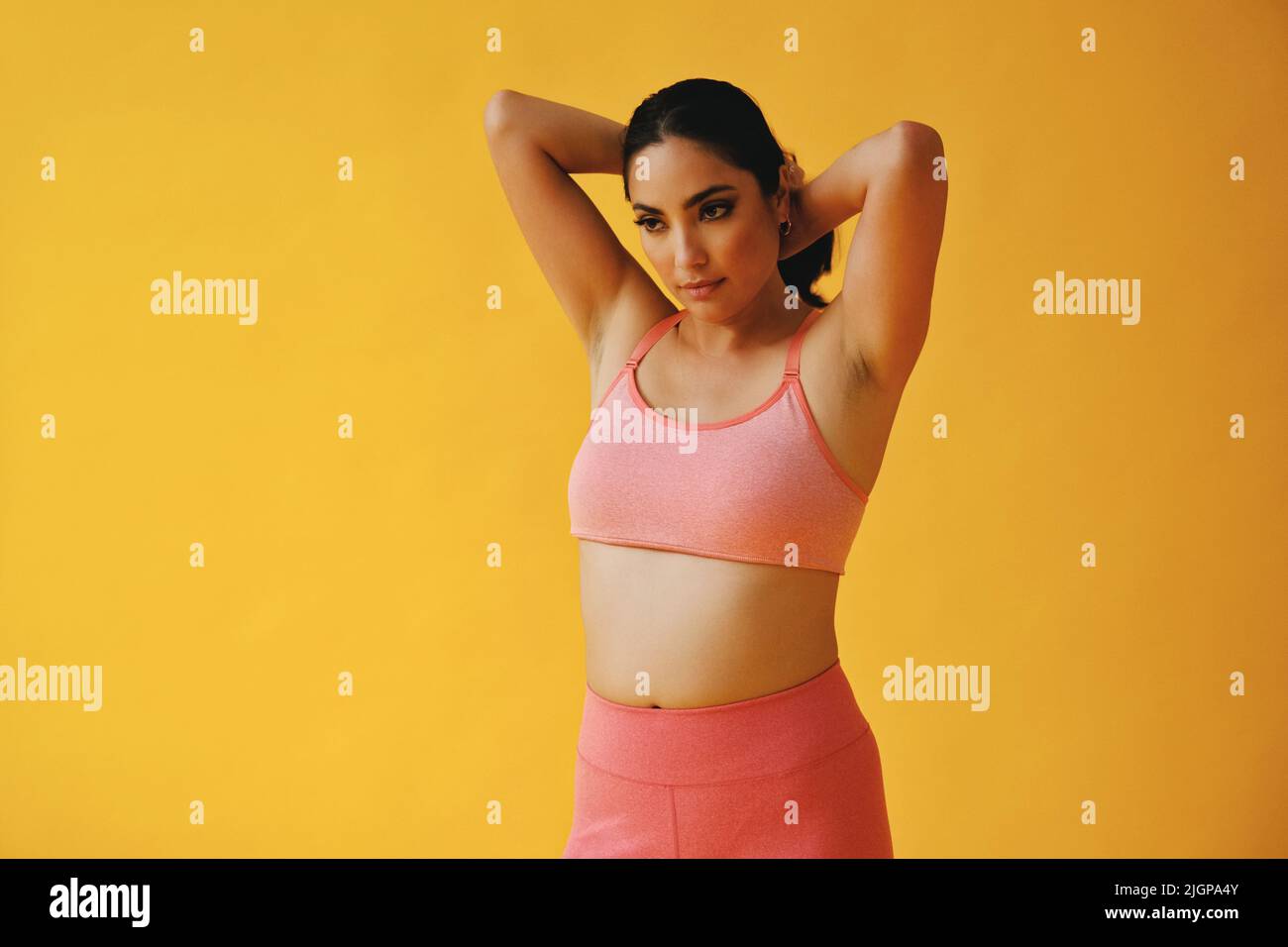 Waist-up-Porträt der hispanischen Schönheit Latina Frau streckt die Hände auf die Haare Sport-Outfit jungen Erwachsenen vor gelbem Hintergrund Blick weg auf Kopie Raum Studio aufgenommen Stockfoto