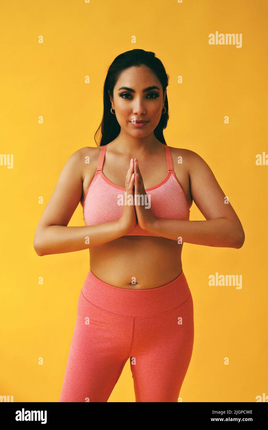 Waist up Porträt der hispanischen Schönheit Latina Frau in Yoga Pose Sport-Outfit jungen Erwachsenen vor gelbem Hintergrund Blick auf Kamera Studio aufgenommen Stockfoto