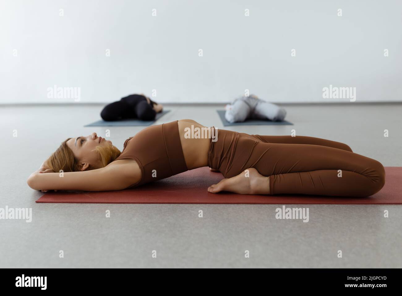 Schlanke junge Frau, die in Supta Virasana liegt, in der Liegenden Heldenpose, die Bauch- und Rückenmuskulatur im Fitnessstudio auf der Matte dehnt Stockfoto