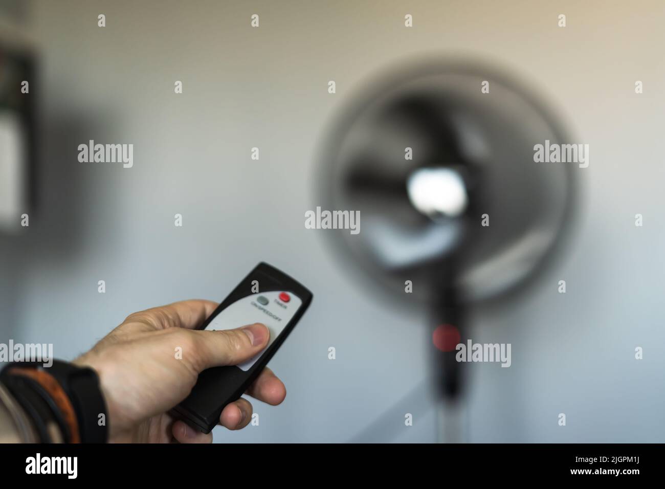 Person, die mitten in einer Hitzewelle einen Ventilator mit einer Fernbedienung anschaltet. Stockfoto