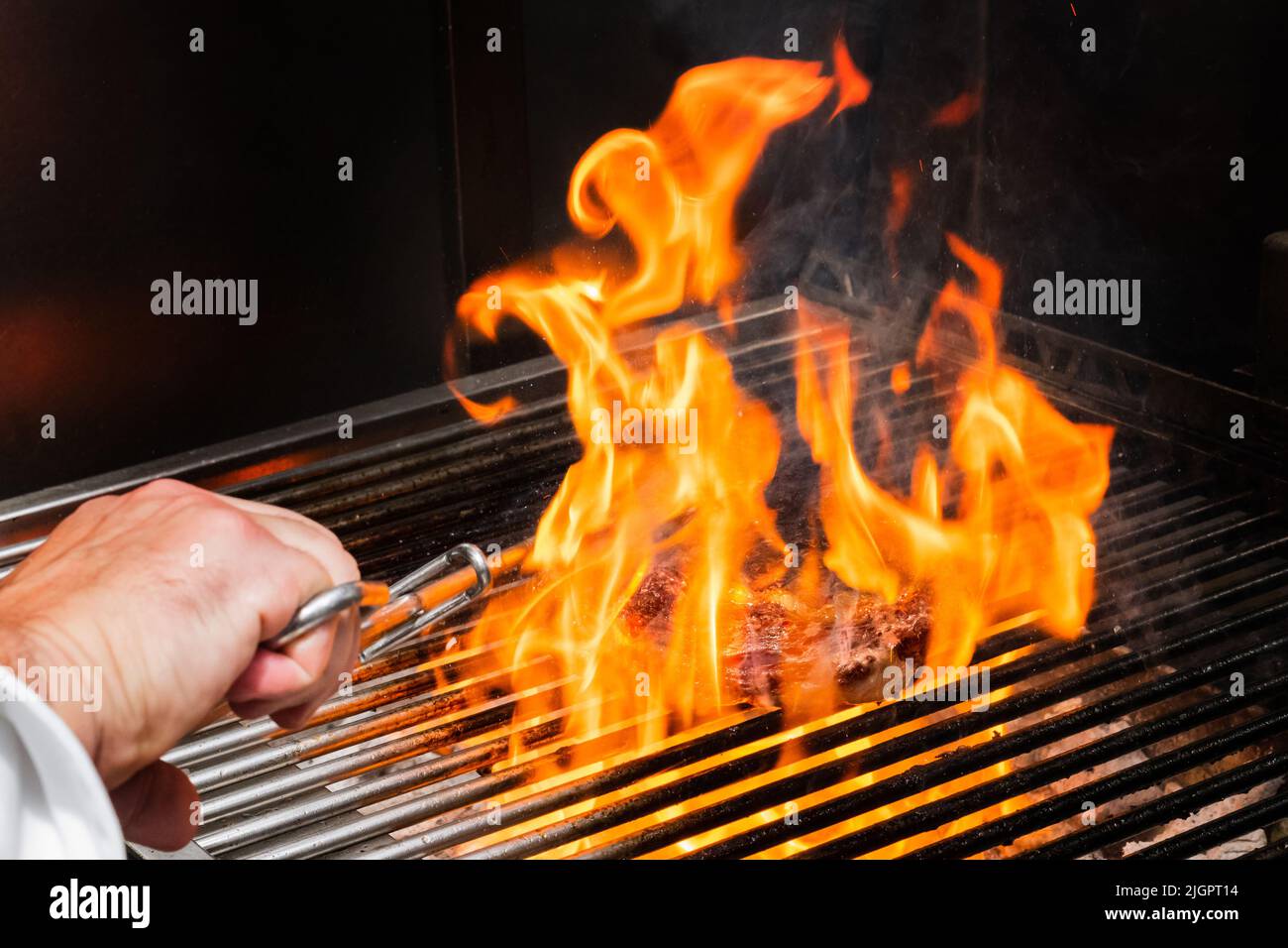 Kalbsschnitzel auf dem Grill mit Feuerflammen und Hand mit Zange Stockfoto