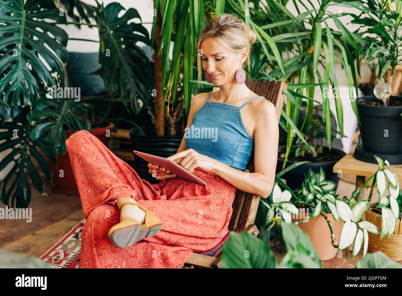 Junge attraktive Geschäftsfrau sitzt zwischen tropischen Topfpflanzen und arbeitet auf digitalen Tablets. Stockfoto