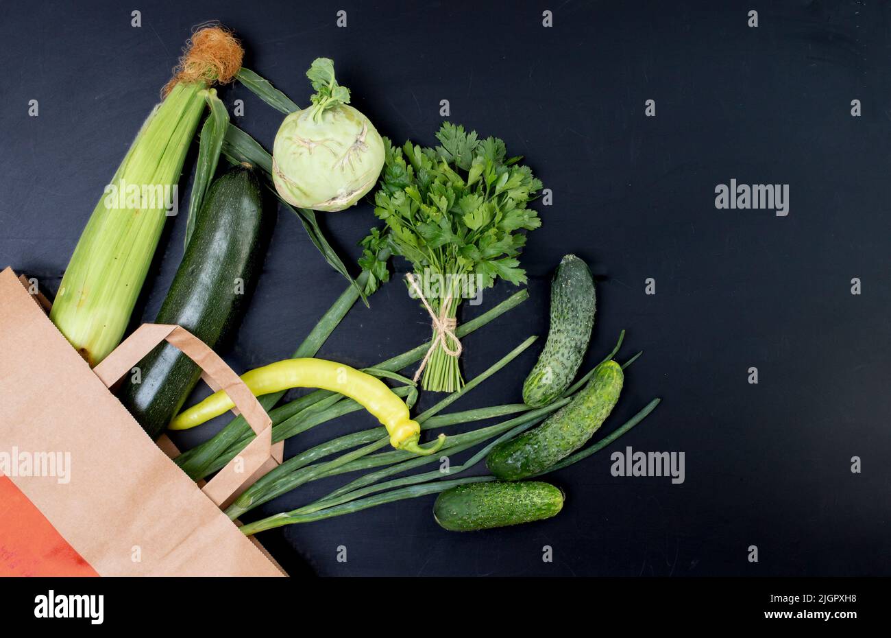 Nur grünes Gemüse kommt aus einer Papiertüte. Vegetarisches Rezepturkonzept. Frühlingszwiebeln, Gurken, Zucchini, Petersilie und Mais, isoliert auf Schwarz Stockfoto