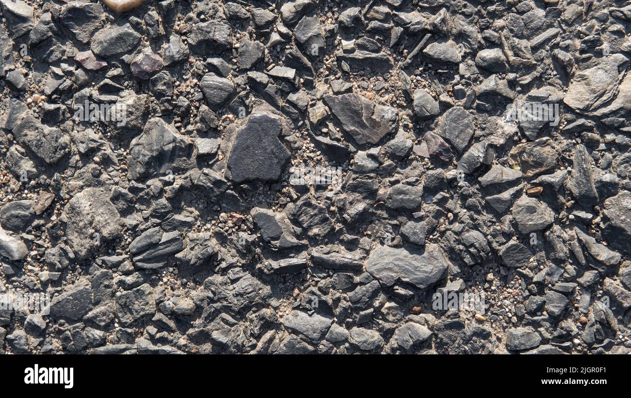 Alte abgestürzte Straße. Schwarze Kieselsteine Hintergrund. Naturstein. Nahaufnahme von Kieselsteinen. Steine im Asphaltboden Stockfoto