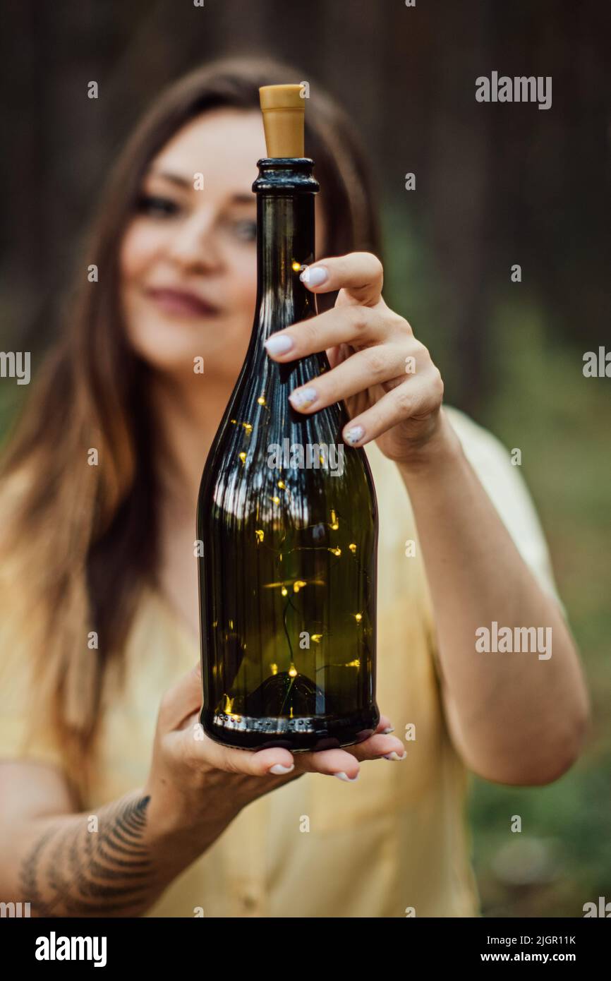 Verzauberung, Magie, Mittsommerritual. Frau mit Farn Tattoo hält Flasche mit Lichtern Stockfoto