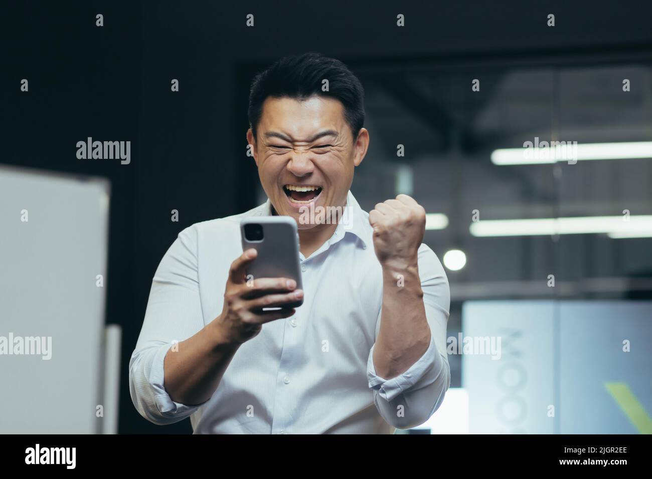 Nahaufnahme Porträt des erfolgreichen asiatischen Geschäftsmannes triumphierend Nachrichten aus dem Telefon lesen, Triumph Erfolg und Sieg feiern, Hand hoch halten Stockfoto