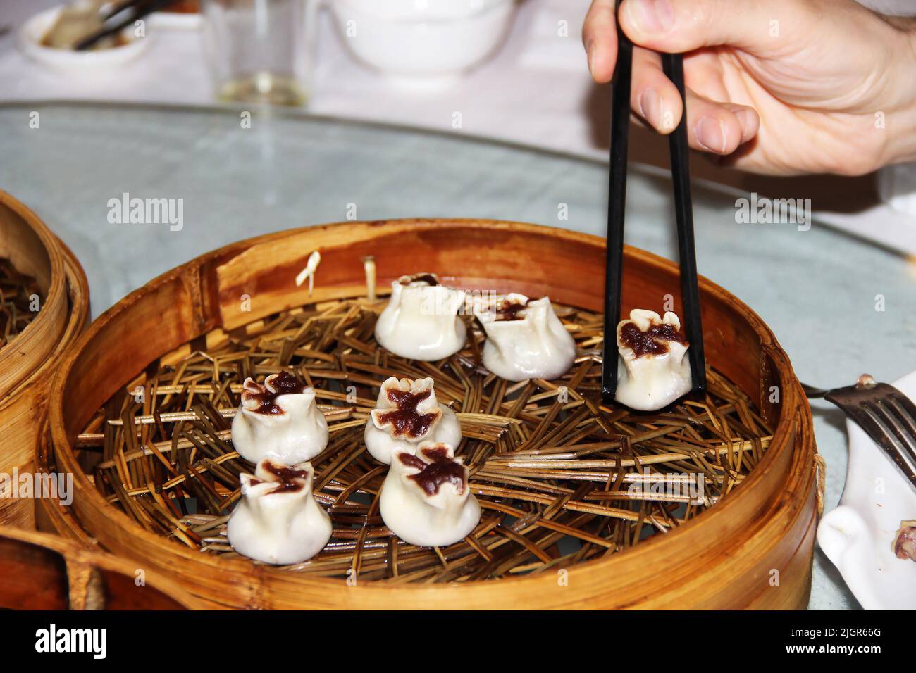 Gekochte Knödel in einem Korbteller auf dem Esstisch. Chinesische Essstäbchen Stockfoto