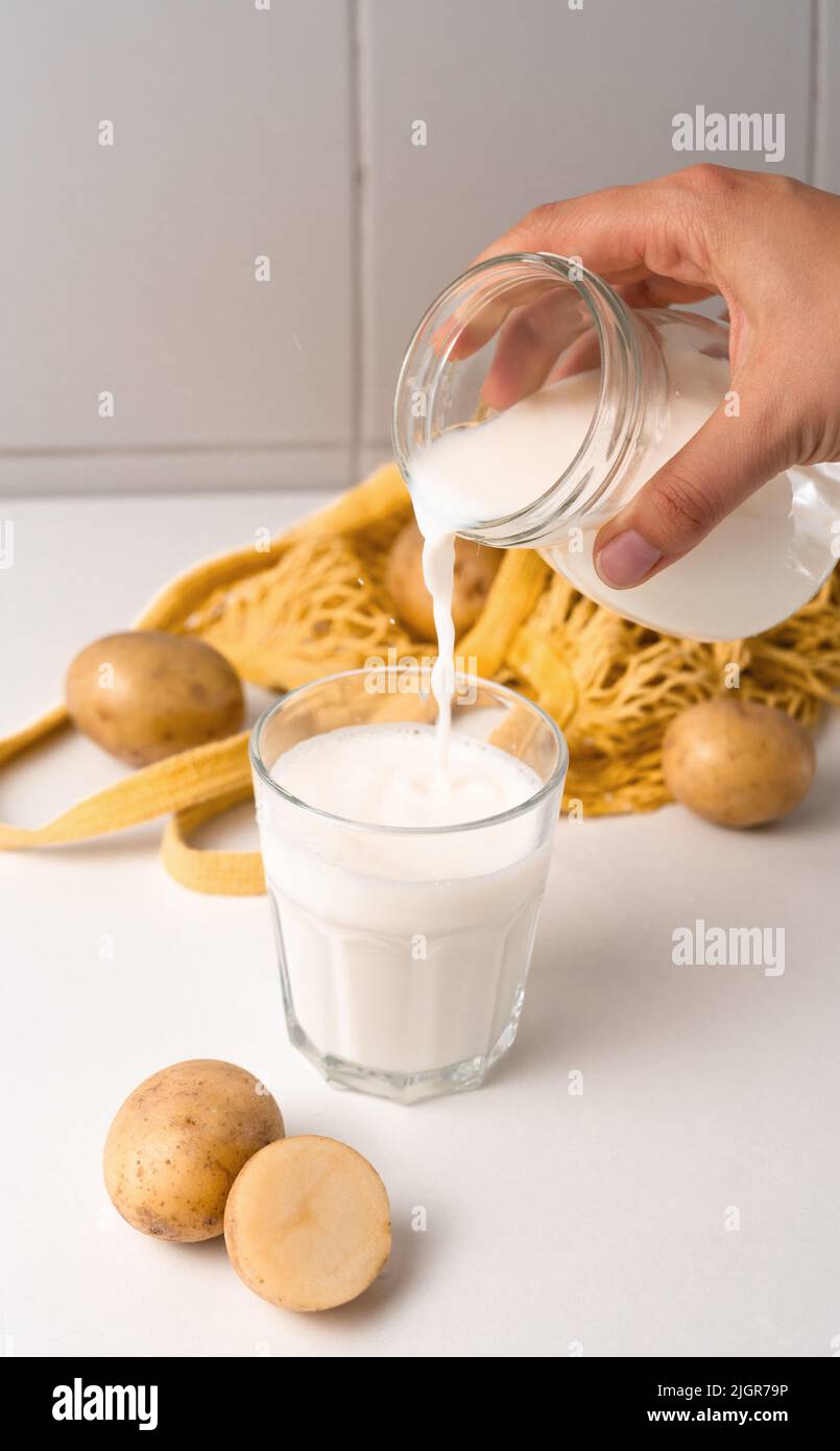 Kartoffelmilch, die auf weißem Tischhintergrund in Glas gießt Stockfoto