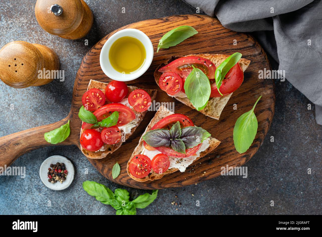 Tomate Ricotta Bruschetta mit Basilikum und Olivenöl auf einem Holzschneidebrett, Draufsicht Stockfoto