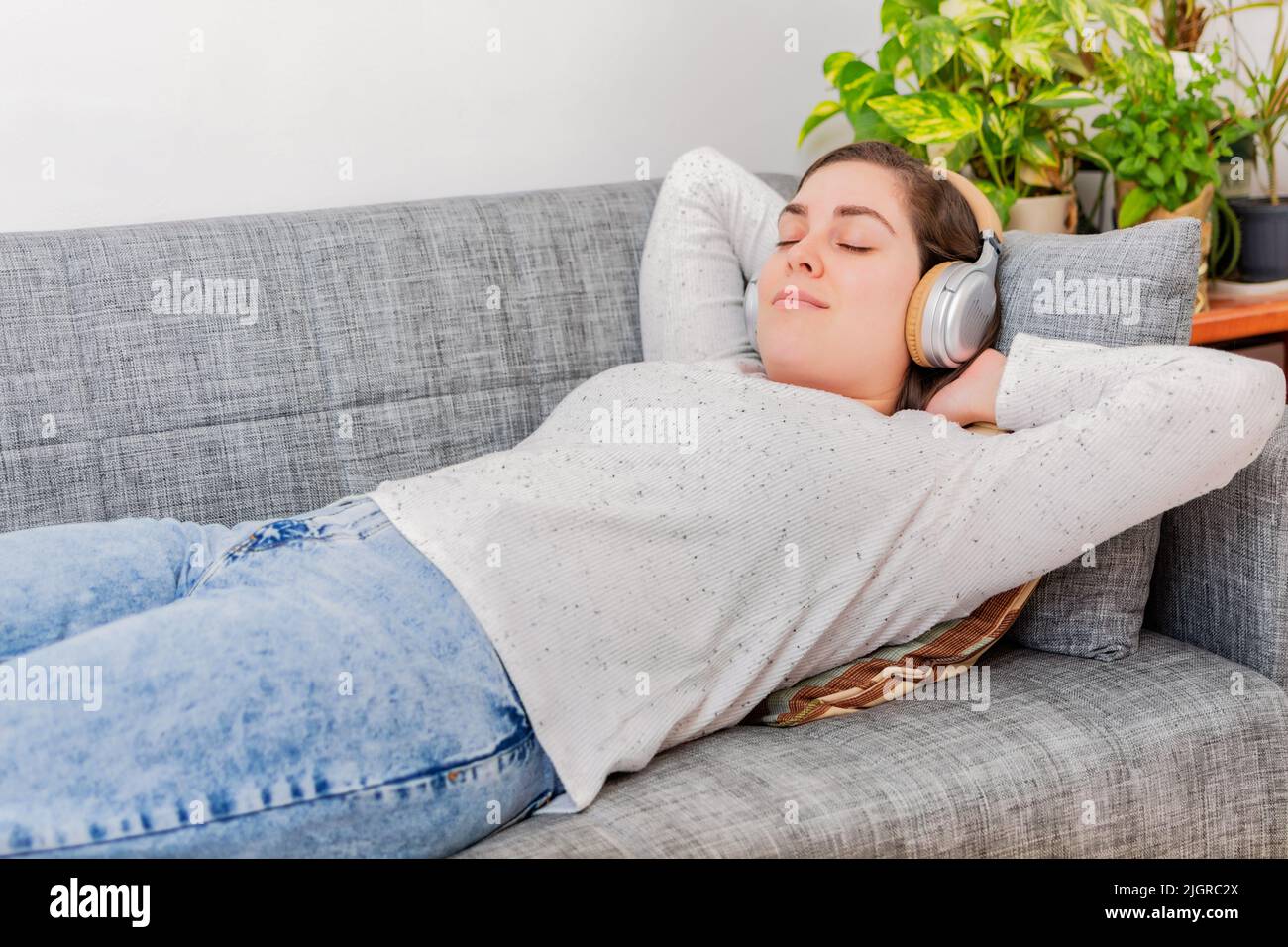 Ein Blick auf eine Frau mit Kopfhörern, die auf der Couch liegt und sich entspannt Stockfoto