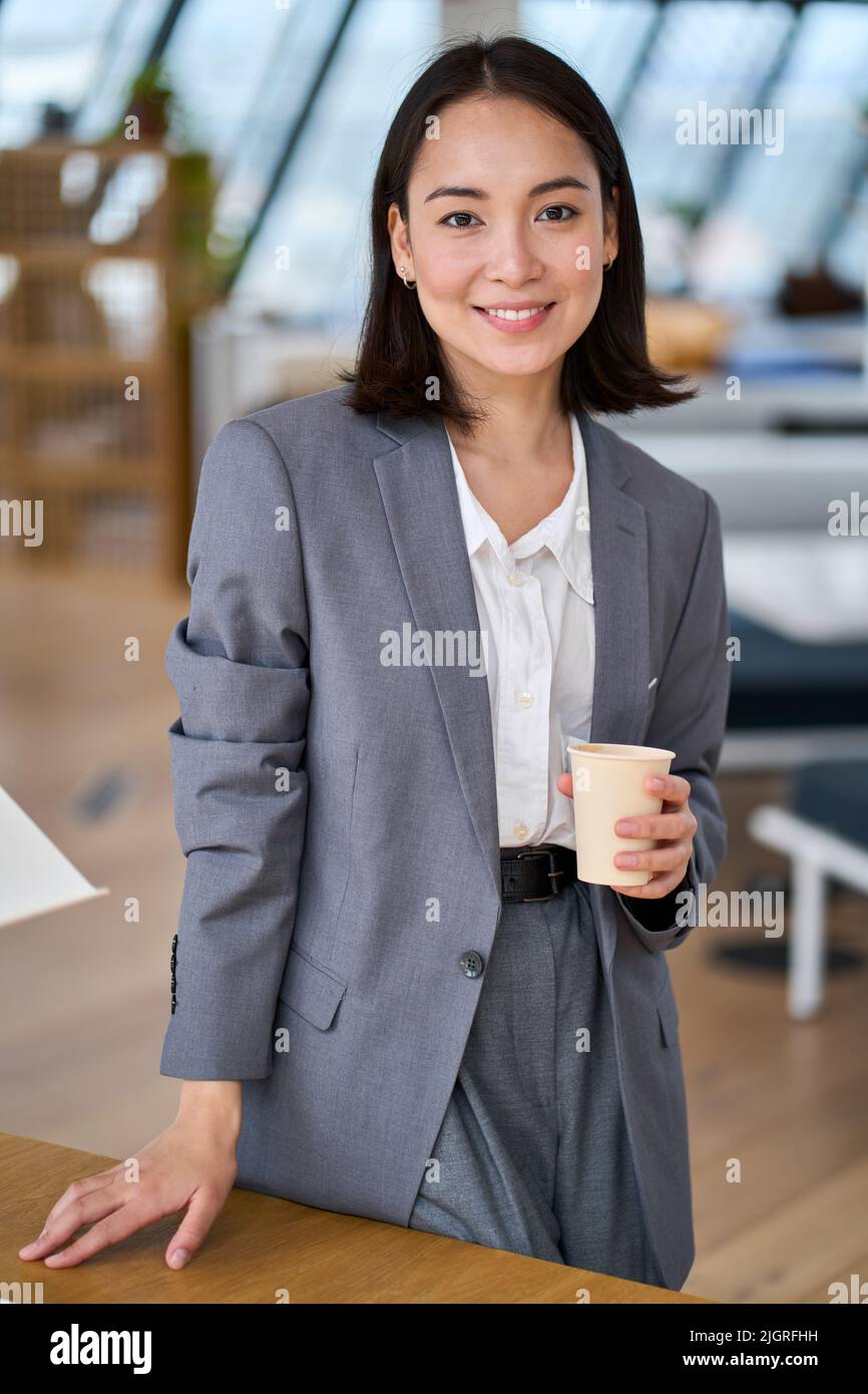 Junge lächelnde asiatische Geschäftsfrau, die im Büro steht. Vertikales Hochformat Stockfoto