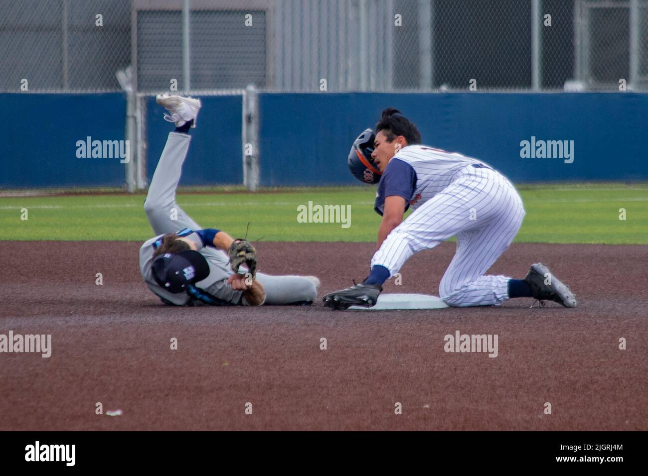 Ein College-Baseballspieler rutscht beim Versuch, zu stehlen, in die zweite Basis, während der zweite Basisspieler den Ball in seinem Baseballhandschuh hält, während er sich überrollt Stockfoto
